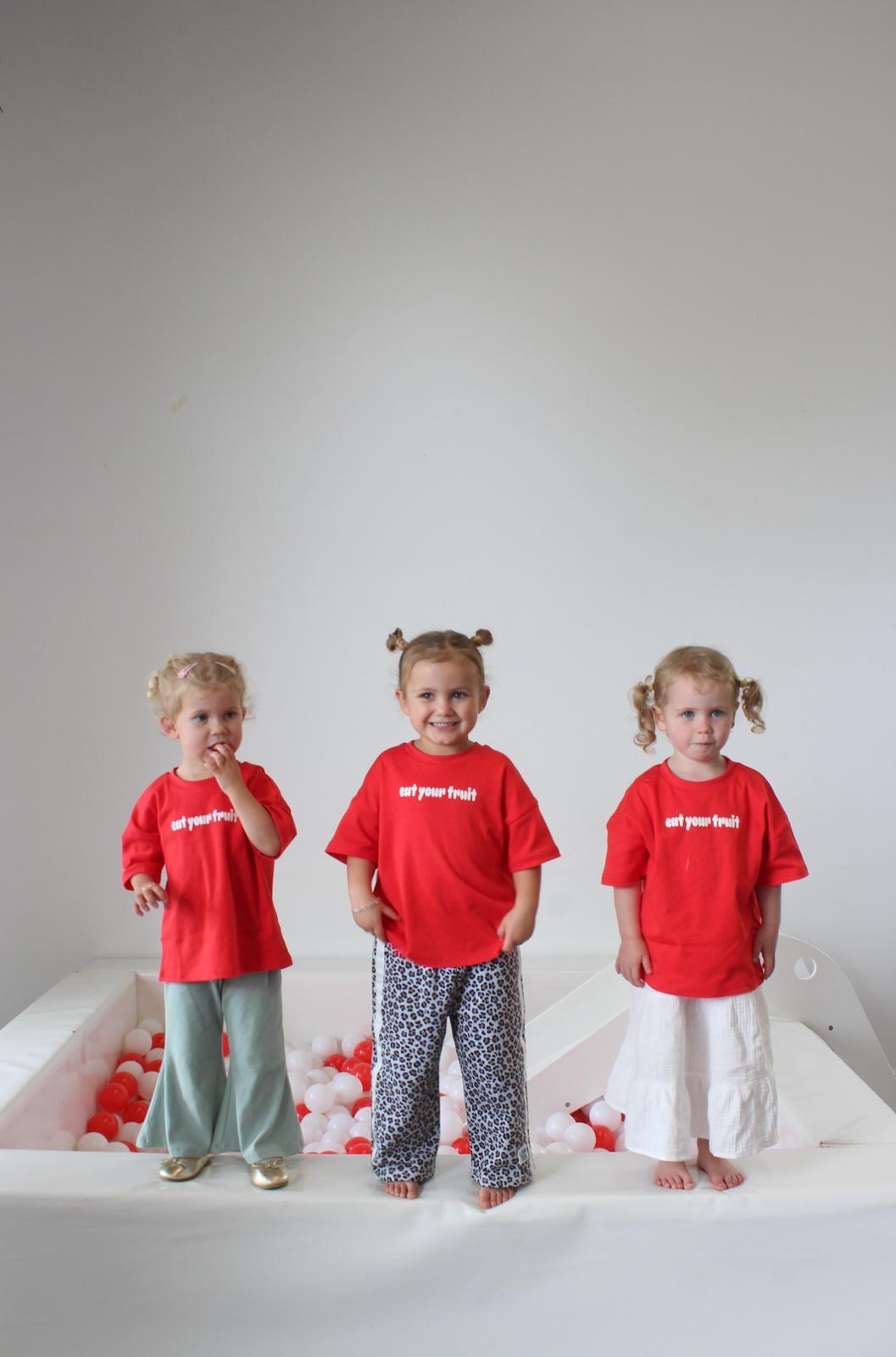 little girls wearing oversized red tshirts with eat your fruit logo and leopard pants