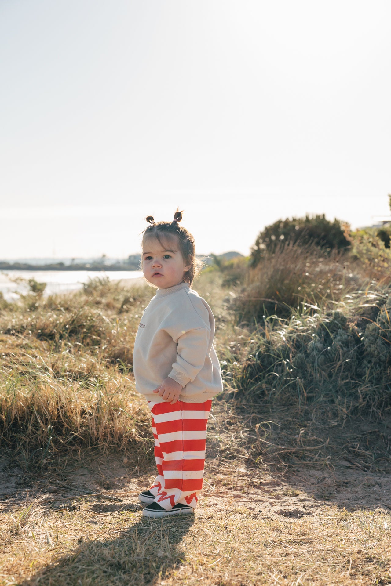 little girl wearing stone jumper and red stripe pants on the beach