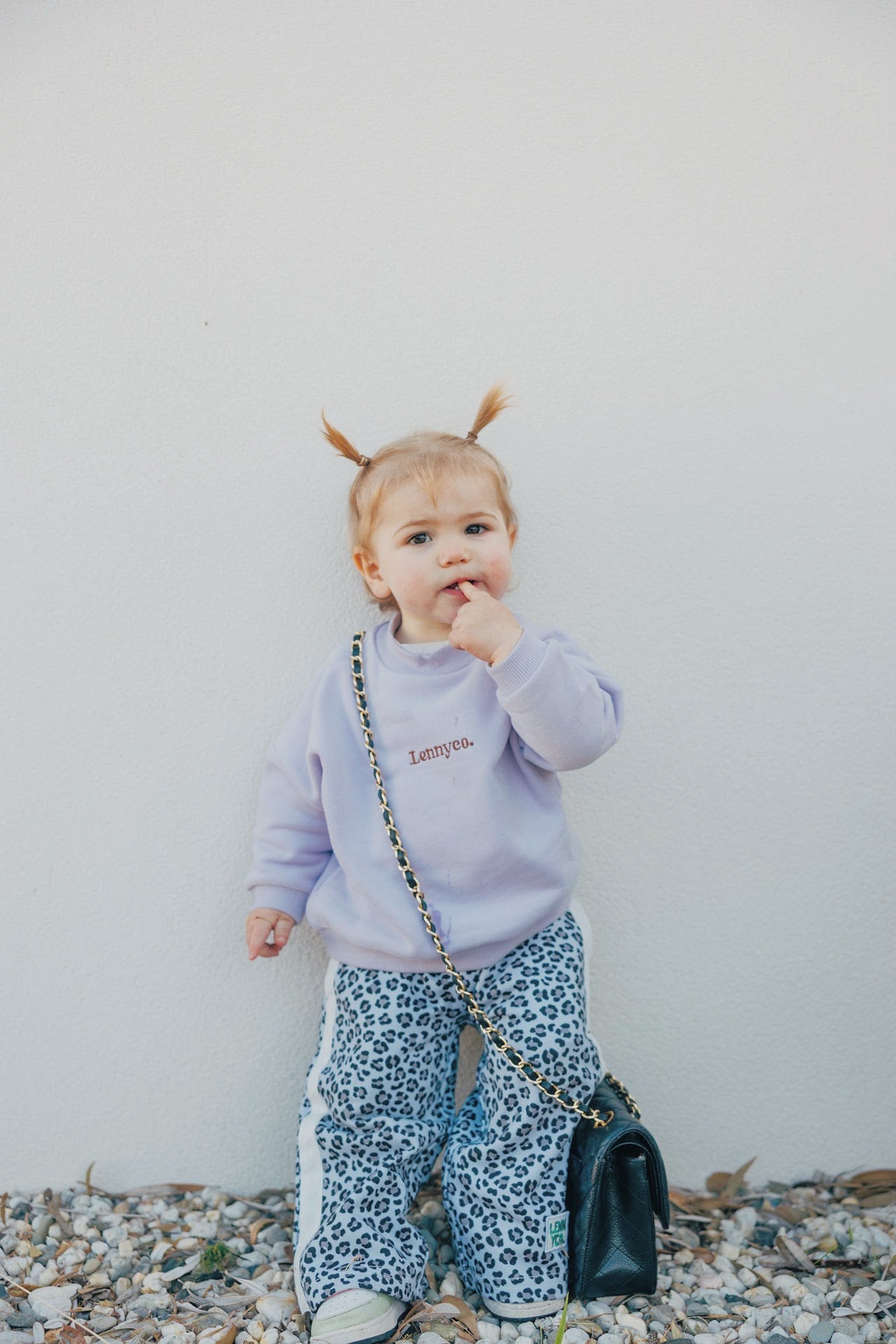 child leaning on wall wearing lilac jumper and leopard pants
