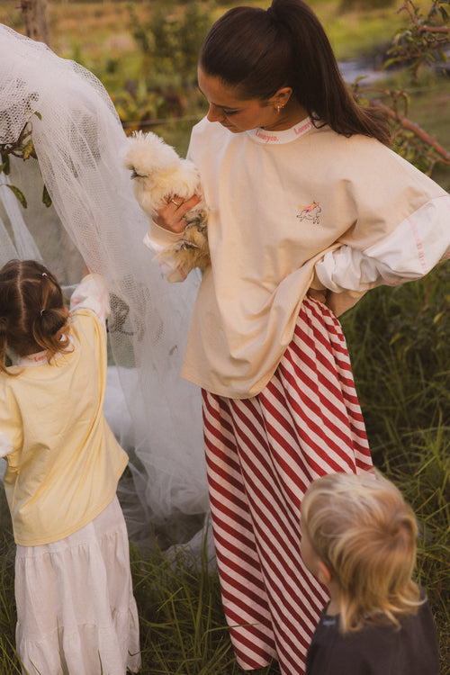 mum wearing unicorn tee with striped red skirt holding chicken on a farm