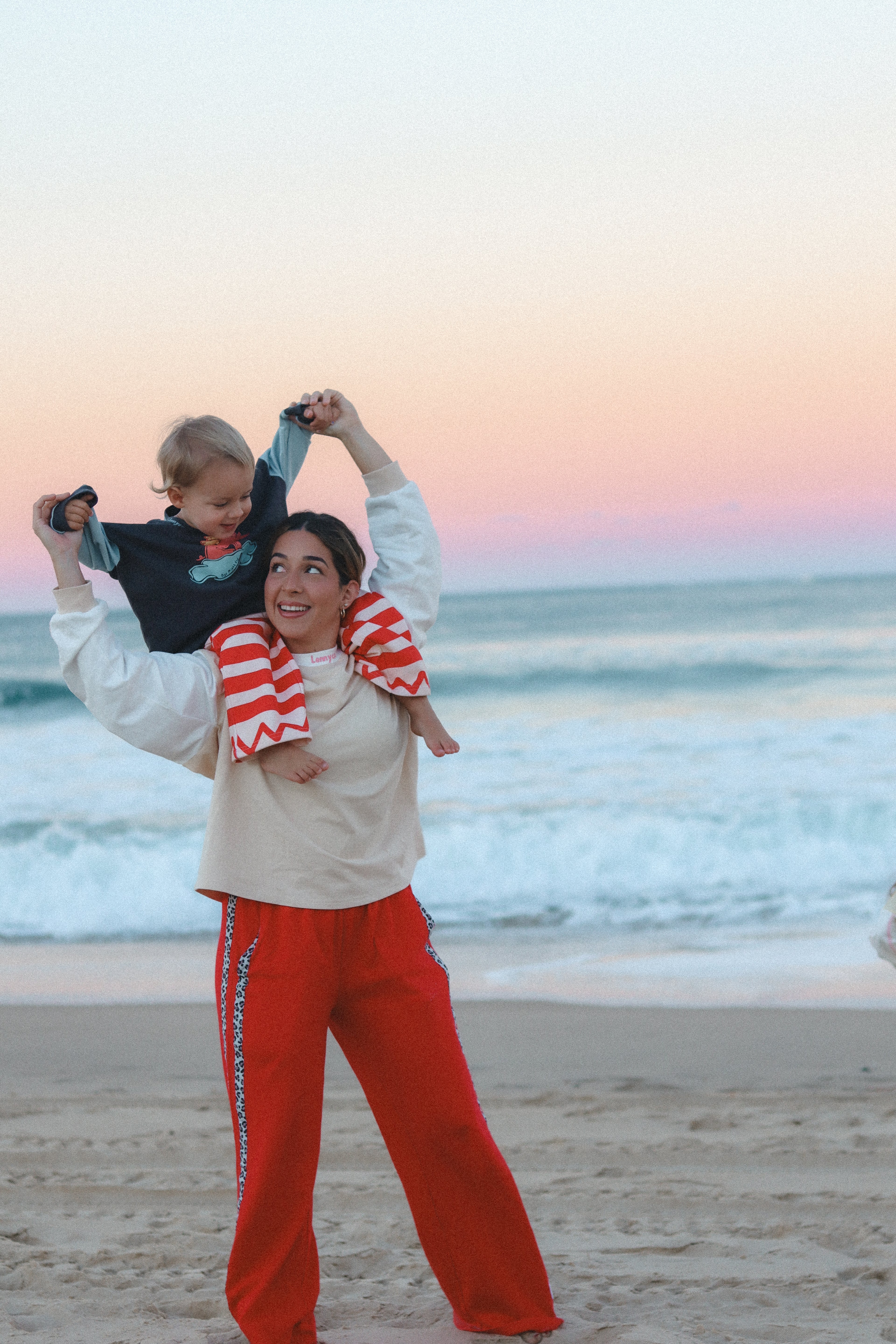 Woman holding a child on a beach with a rainbow in the sky