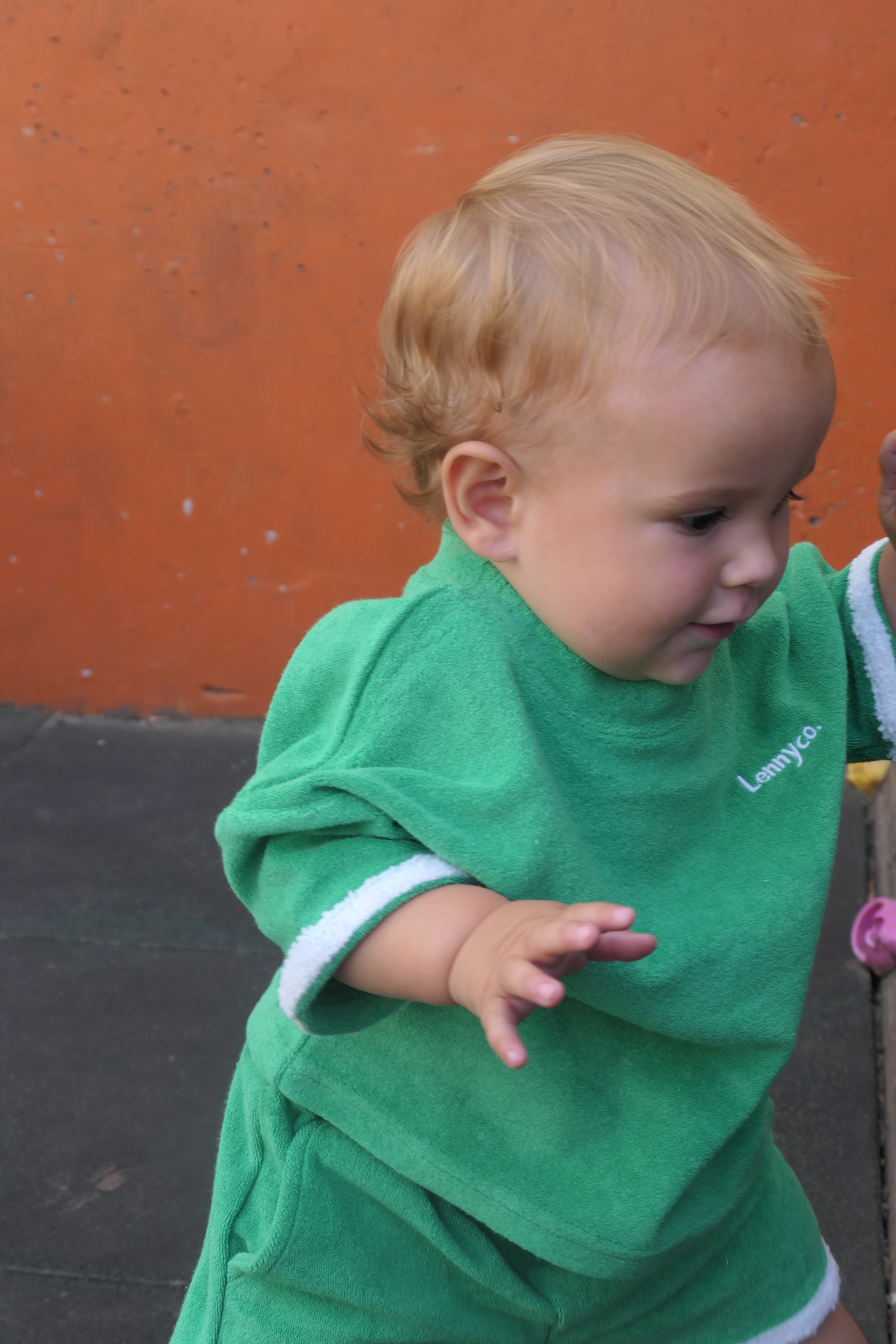 baby in a green terry towelling set with white trim against an orange wall play area