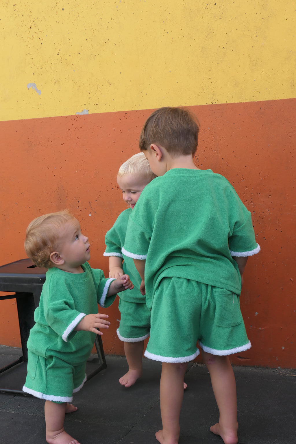Three children in green outfits playing on a colorful playground surface.